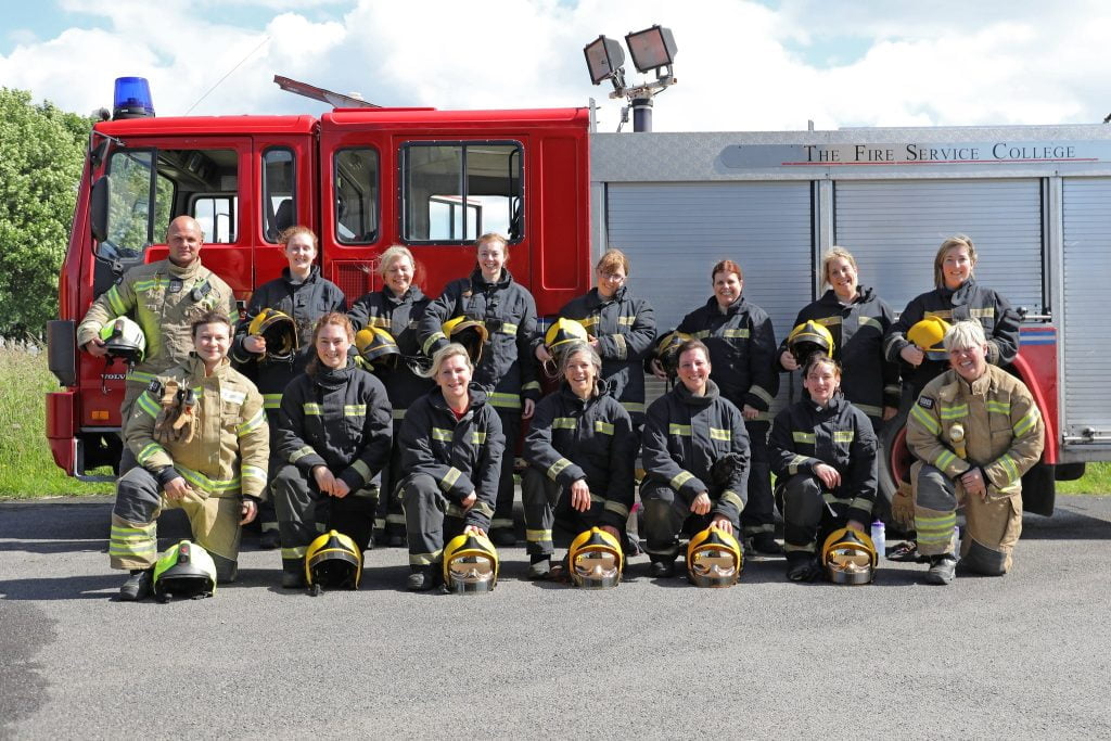 Fifteen people standing or kneeling in fire kit in front of a fire appliance