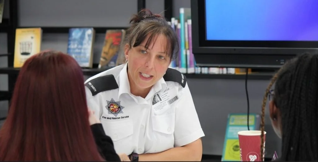 Daisy Byron in white service uniform speaking with two young women in a school setting