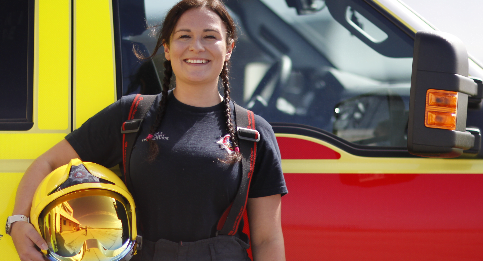 Airport Firefighter wearing firefighter kit and holding a protective yellow helmet whilst standing in front of a fire appliance